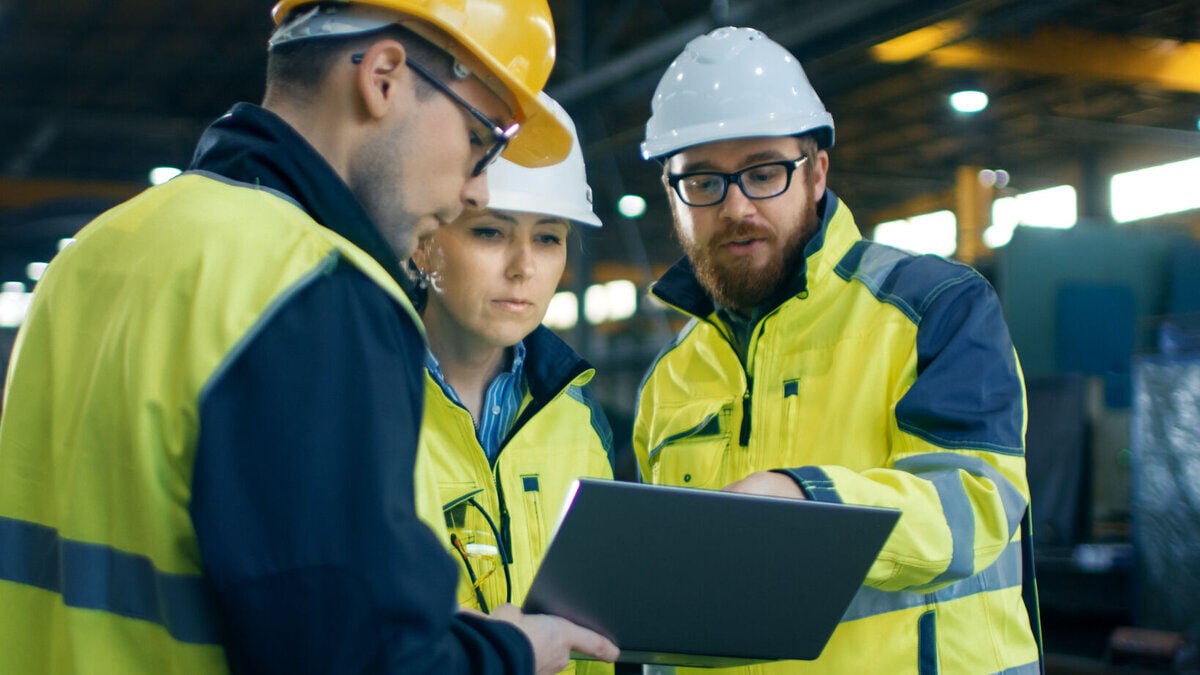 Three workers wearing construction hats looking at a laptop 