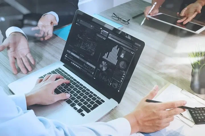 business%20documents%20on%20office%20table%20with%20smart%20phone%20and%20laptop%20computer%20and%20graph%20financial%20with%20social%20network%20diagram%20and%20three%20colleagues%20discussing%20data%20in%20the%20background.webp?width=720&height=480&name=business%20documents%20on%20office%20table%20with%20smart%20phone%20and%20laptop%20computer%20and%20graph%20financial%20with%20social%20network%20diagram%20and%20three%20colleagues%20discussing%20data%20in%20the%20background.webp